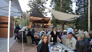 An outdoor dining area with tables and chairs, a stage with string lights, and a canopy overhead. - Arrowhead Mountain Lodge (Cimarron)