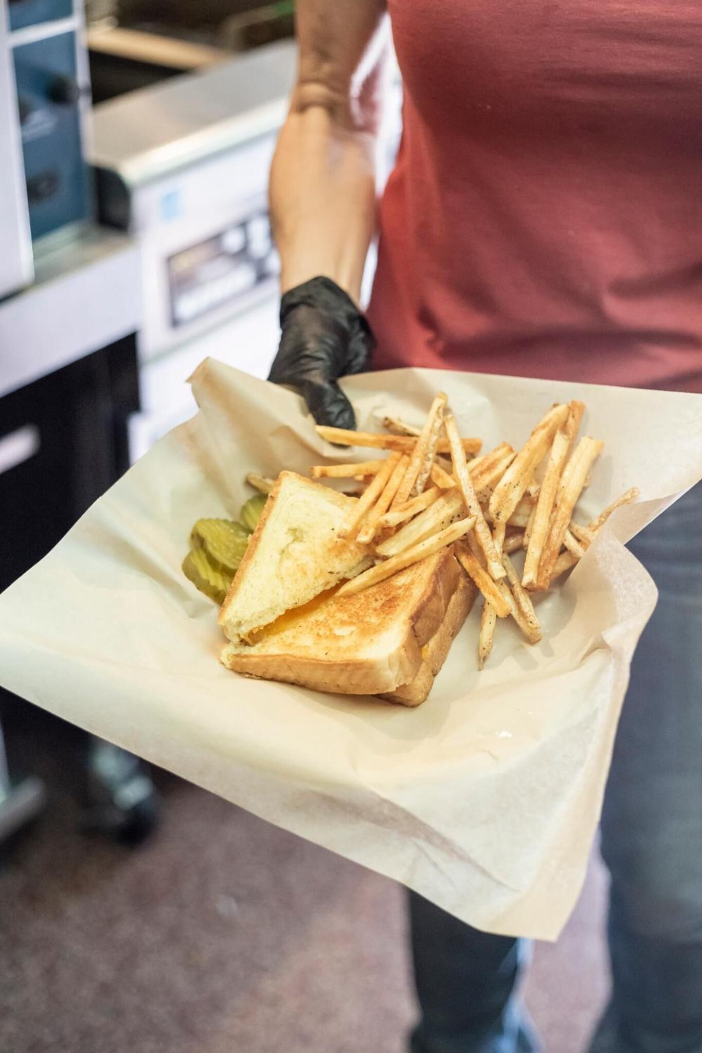Un sándwich con papas fritas y pepinillos en una bandeja de papel.