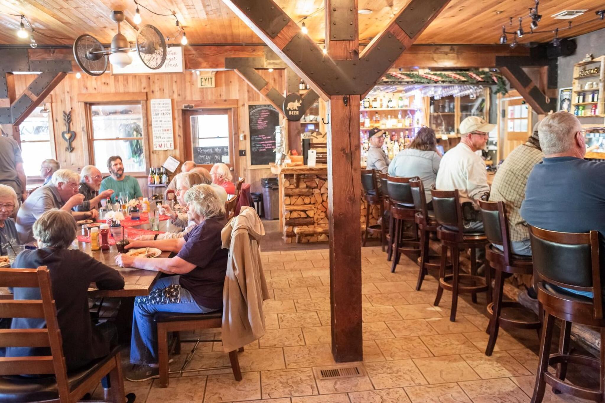 A rustic interior with wooden beams, a bar area, and patrons dining at tables.