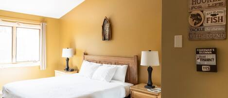 Une chambre d’hôtel comprenant un lit, deux tables de chevet avec des lampes, une fenêtre et des éléments de décoration murale, notamment des panneaux avec des expressions liées à la pêche.