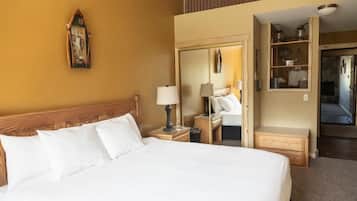 Ein Hotelzimmer mit einem großen Bett, einem Nachttisch mit Lampe, einem Holz-Kopfteil, einem Spiegel und einem Regal mit Küchenutensilien.