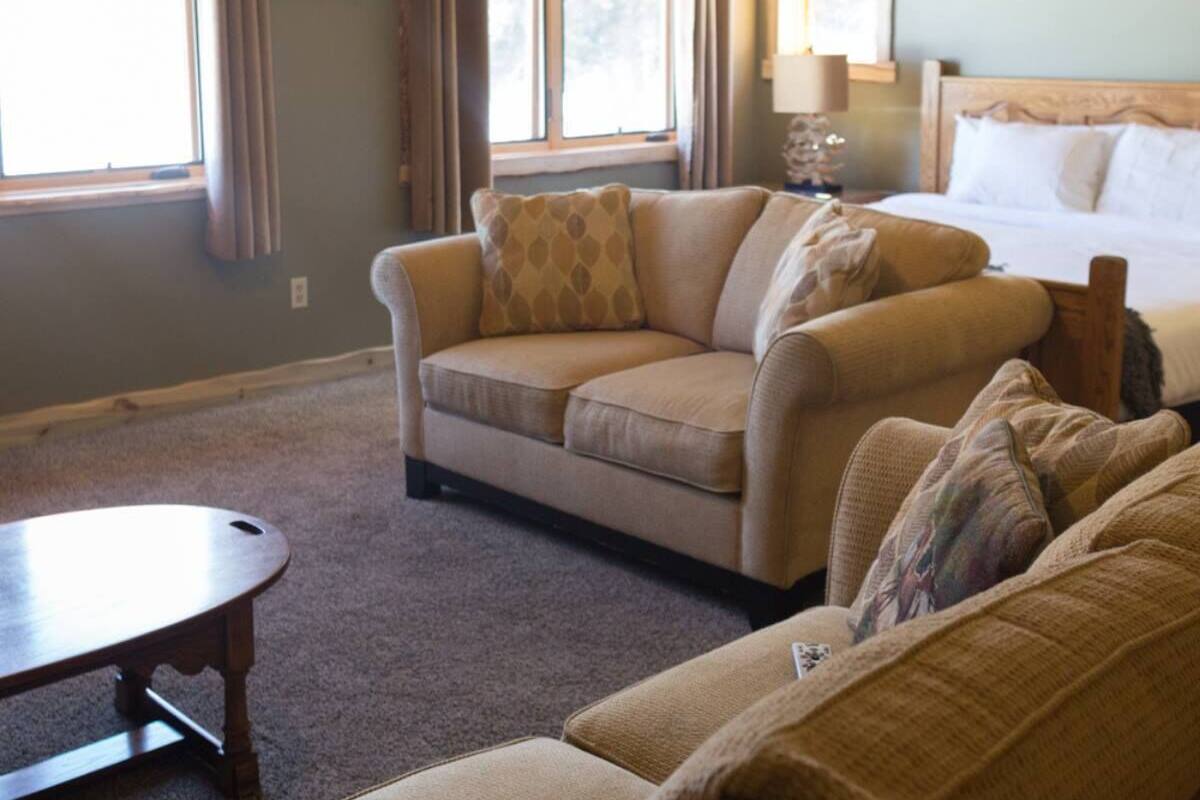 Una habitación acogedora con una cama, dos sofás, una mesita y ventanas amplias.
