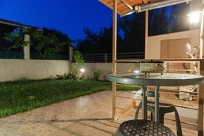 An outdoor patio area with a round metal table and a stool, surrounded by a low wall and a garden.