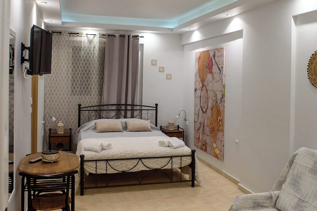 A bedroom with a bed, bedside tables, a chair, a TV mounted on the wall, and a large abstract painting.