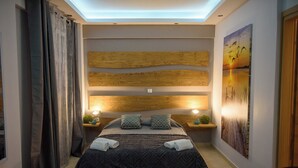 Un dormitorio moderno con cabecera de madera, una cama grande con ropa de cama estampada, dos mesitas de noche con lámparas y un cuadro grande en la pared.