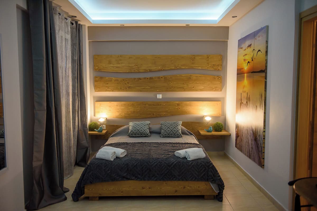 A modern bedroom with a wooden headboard, a large bed with patterned bedding, two bedside tables with lamps, and a large wall painting.