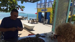 A beachside restaurant with a view of the sea, a table with food, and a person preparing food. - MTB  & Beach House in Cabo Rojo (boqueron)