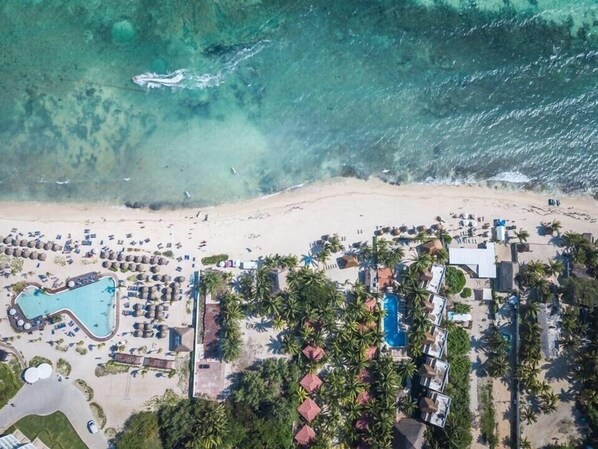 Oversigtsbillede af et strandresort med swimmingpool, strandparasoller og palmer.