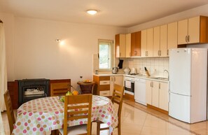 Une cuisine compacte avec des meubles en bois, un réfrigérateur blanc, une table à manger recouverte d’une nappe à pois et un petit poêle.