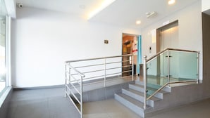 Un escalier moderne avec des rampes en verre et des mains courantes en métal, menant à un ascenseur.