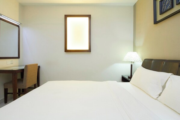 A hotel room with a bed, a desk, a chair, a lamp, and a framed picture on the wall.
