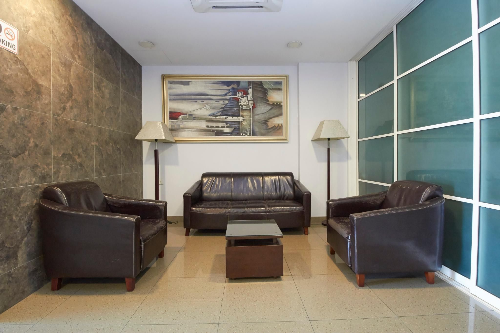 A lobby with a dark leather sofa, two armchairs, a coffee table, and a painting on the wall.