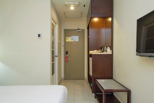 A narrow hotel corridor with a bed on the left, a wooden bench, and a TV mounted on the wall. - Hotel Kepong (Kuala Lumpur)