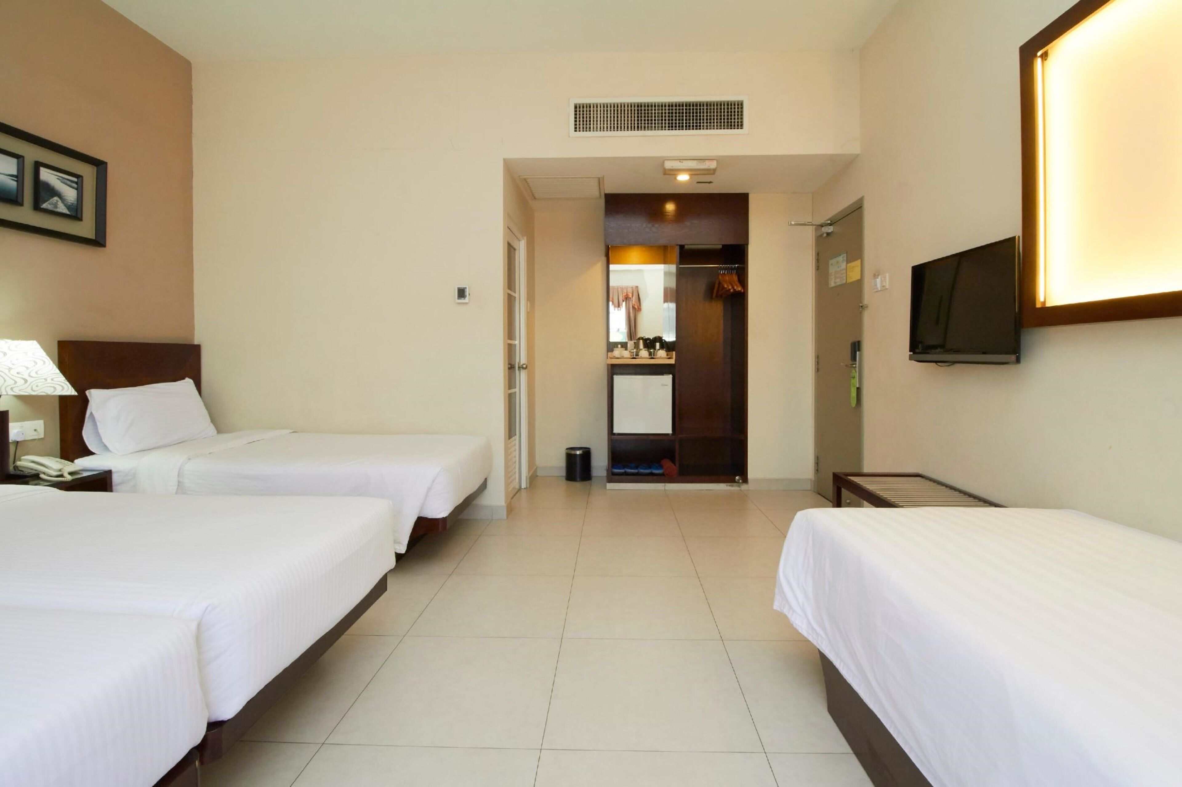 A hotel room with two beds, a TV mounted on the wall, and a small desk with a lamp.