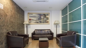 Un hall d’entrée avec un canapé en cuir marron, deux fauteuils, une petite table basse et un tableau accroché au mur.