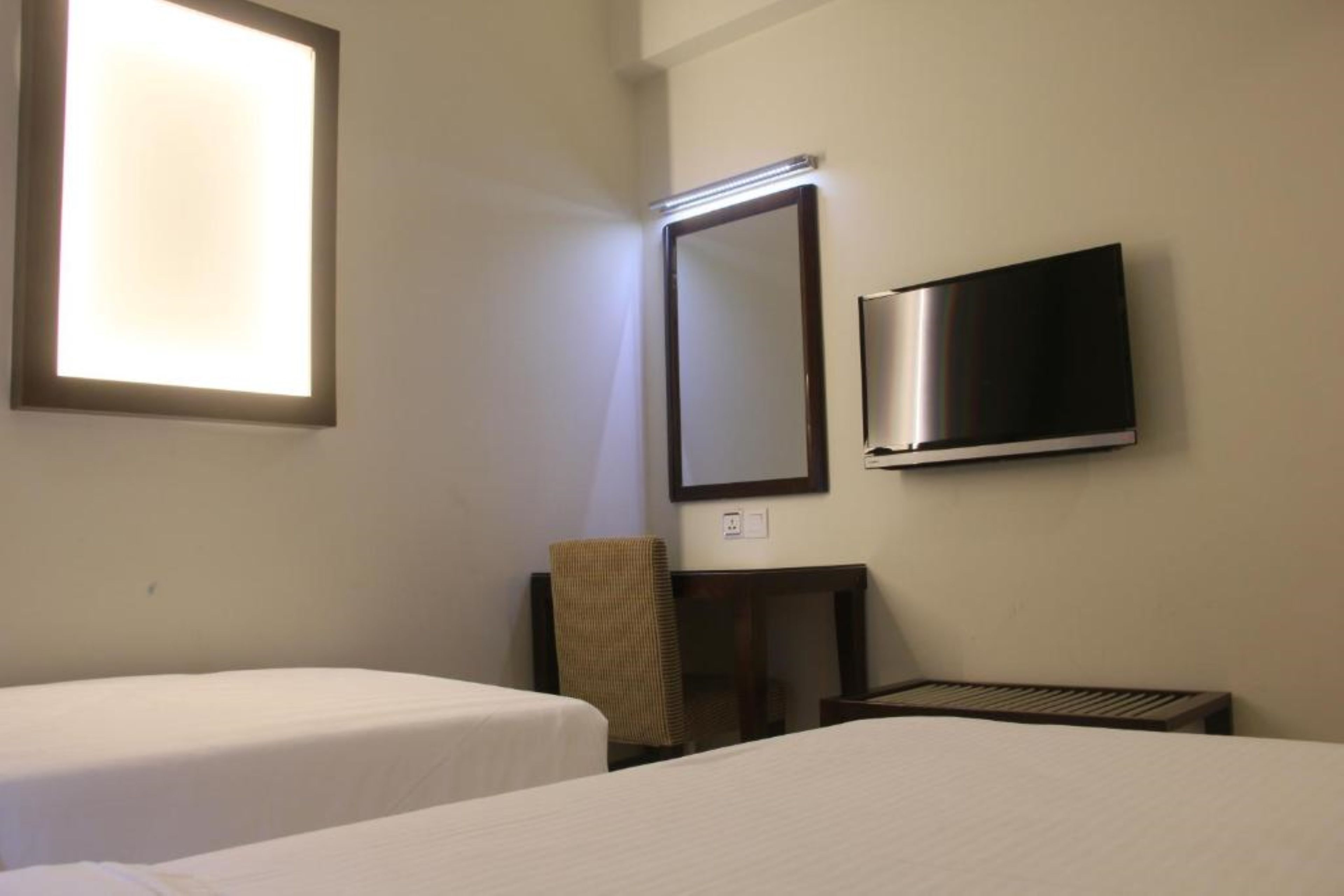 A hotel room with two single beds, a flat-screen TV mounted on the wall, a small table, and a chair.
