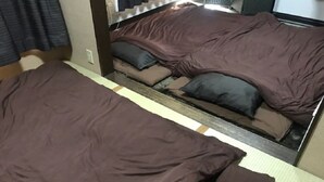 A double bed with a brown cover and pillows, a bedside table, and a window with curtains. - Ever Garden (Miyoshi)