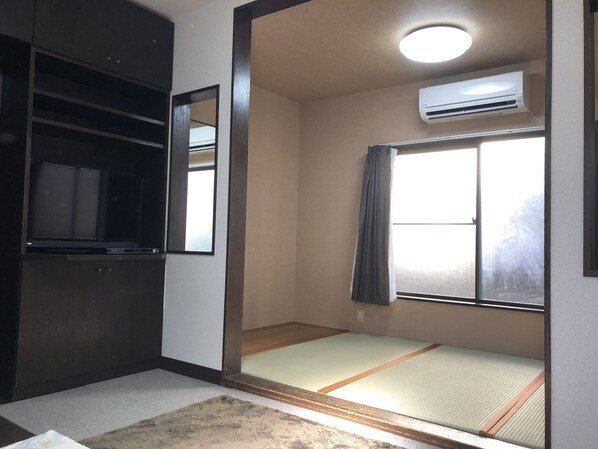 A room with a tatami mat floor, a sliding door, a ceiling fan, and an air conditioning unit.