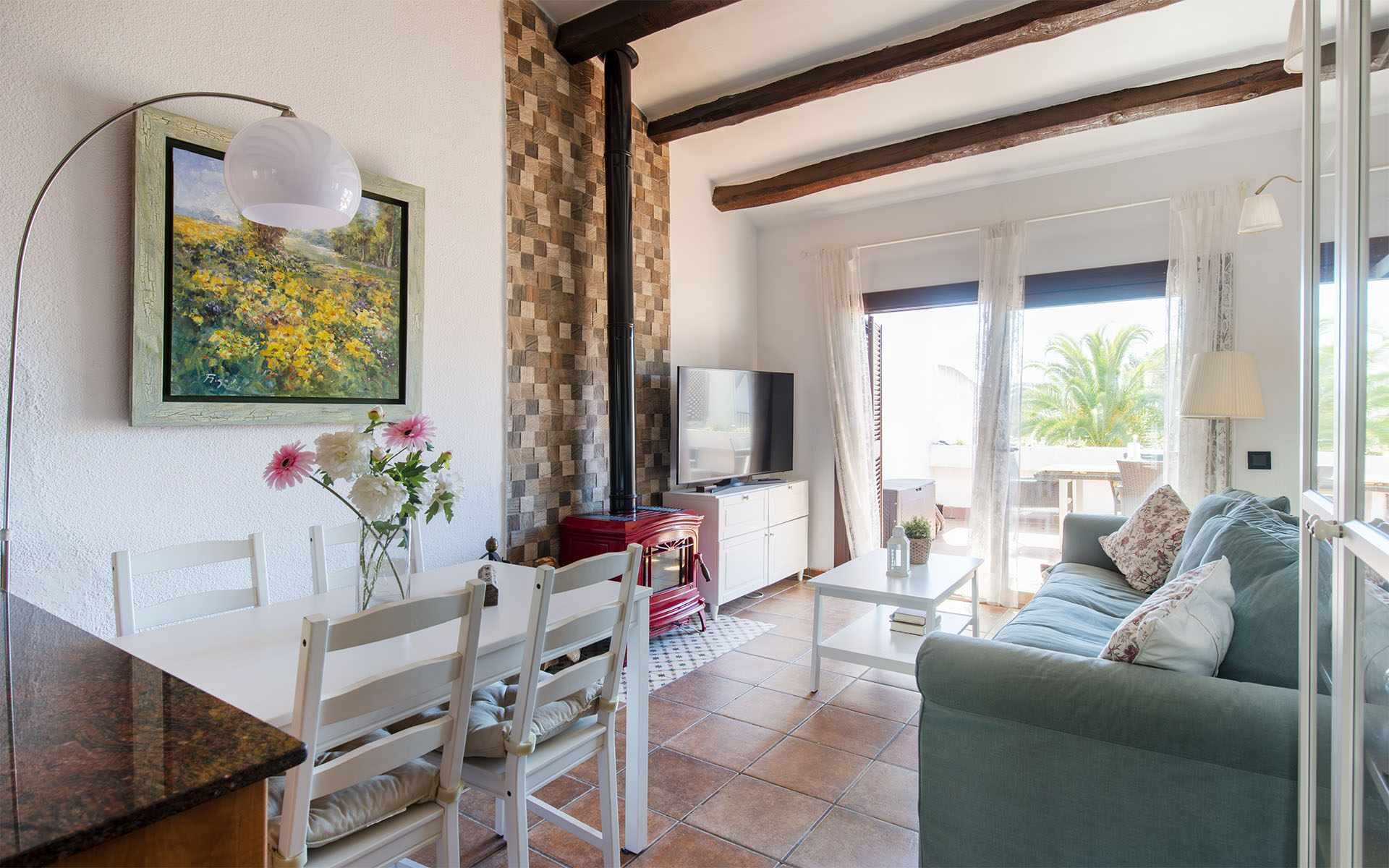 Een gezellige woonkamer met een eethoek, een televisie en een groot raam met uitzicht op palmbomen.