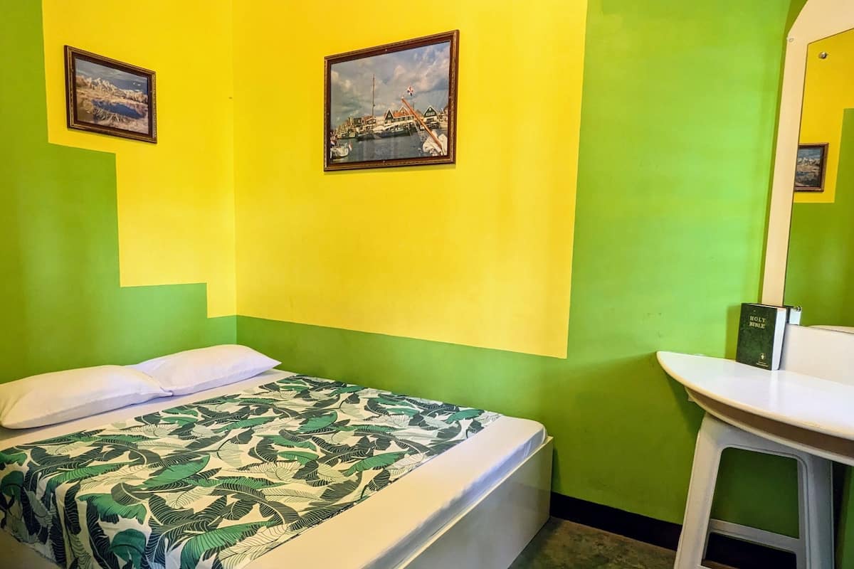Ein Zimmer mit einem Bett, einem weißen Waschbecken und zwei gerahmten Bildern an den Wänden.