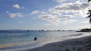 Uma praia com barcos na água e uma pessoa nadando.