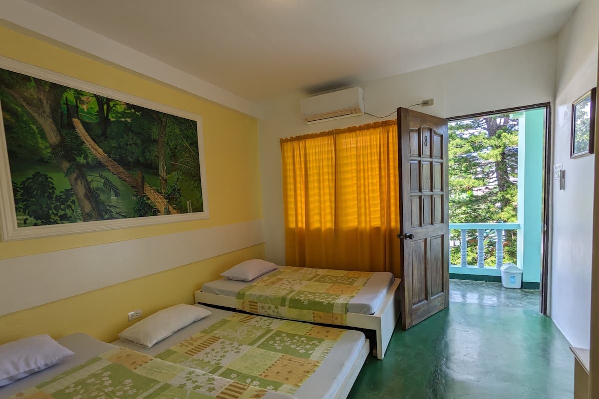 Ein Zimmer mit zwei Betten, einem Waldgemälde, einem fenster mit Vorhängen und einer Tür, die auf einen Balkon führt.