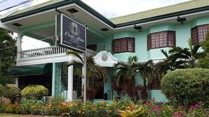Um edifício de dois andares com uma placa indicando Citadel Luna, apresentando uma varanda e um jardim com diversas plantas e flores.