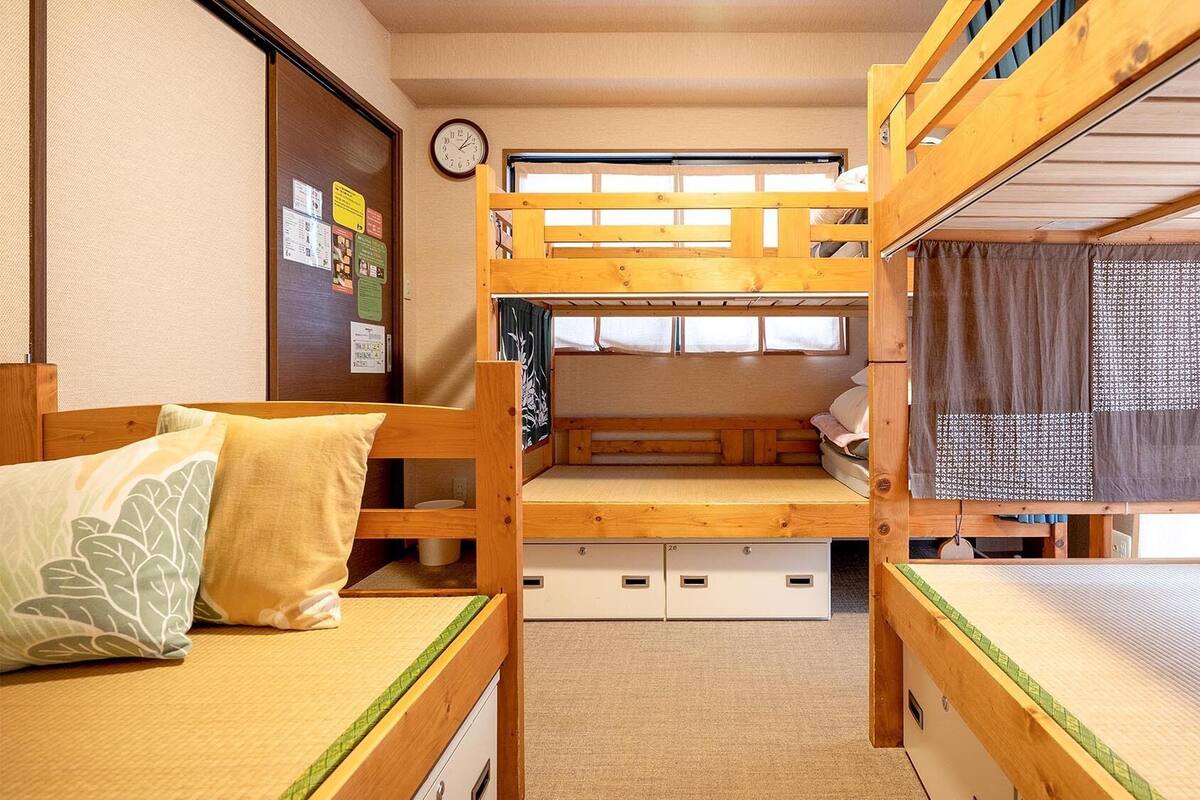 Une chambre avec un lit superposé, une tête de lit en bois, une horloge au mur et une fenêtre avec un rideau.