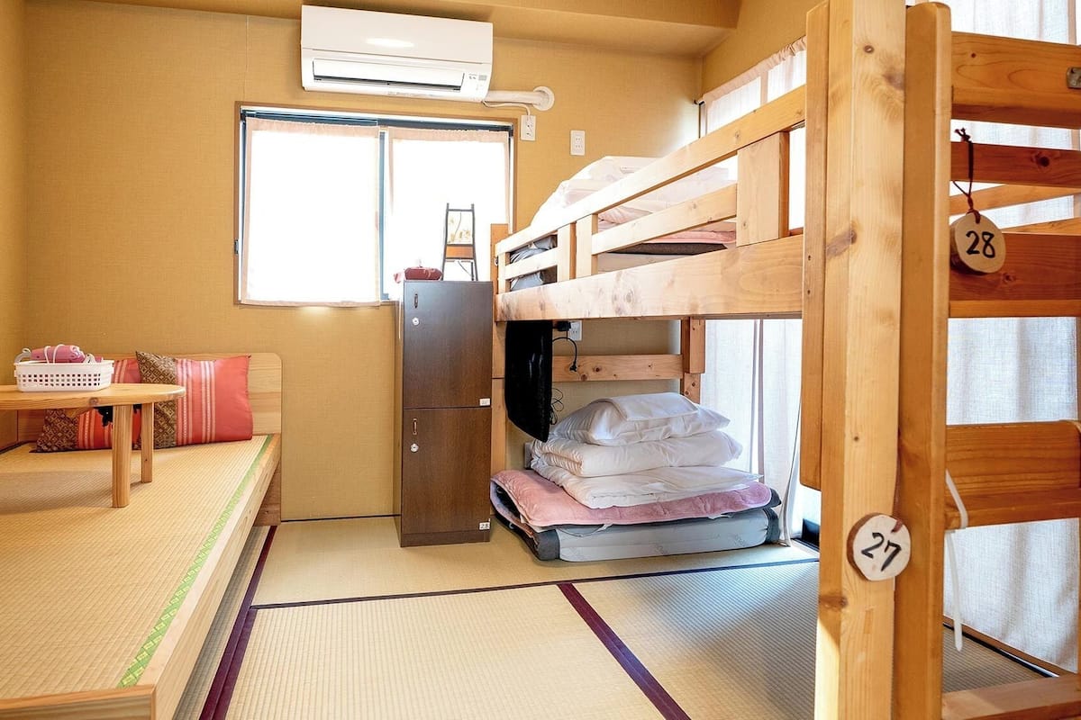 Une chambre de dortoir avec des lits superposés, une petite table, un réfrigérateur et une fenêtre.