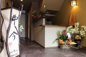 A reception area with a reception desk, a signboard, and various potted plants.