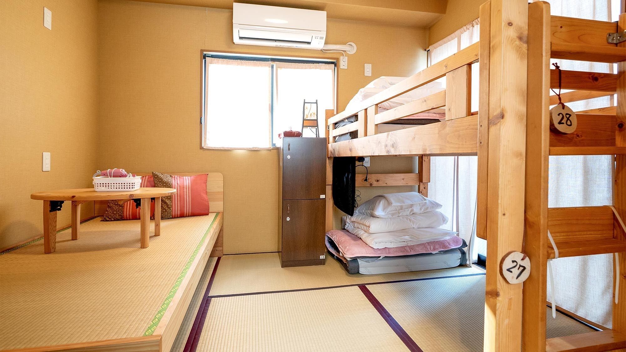 A bunk bed room with a small table, a refrigerator, and a window.