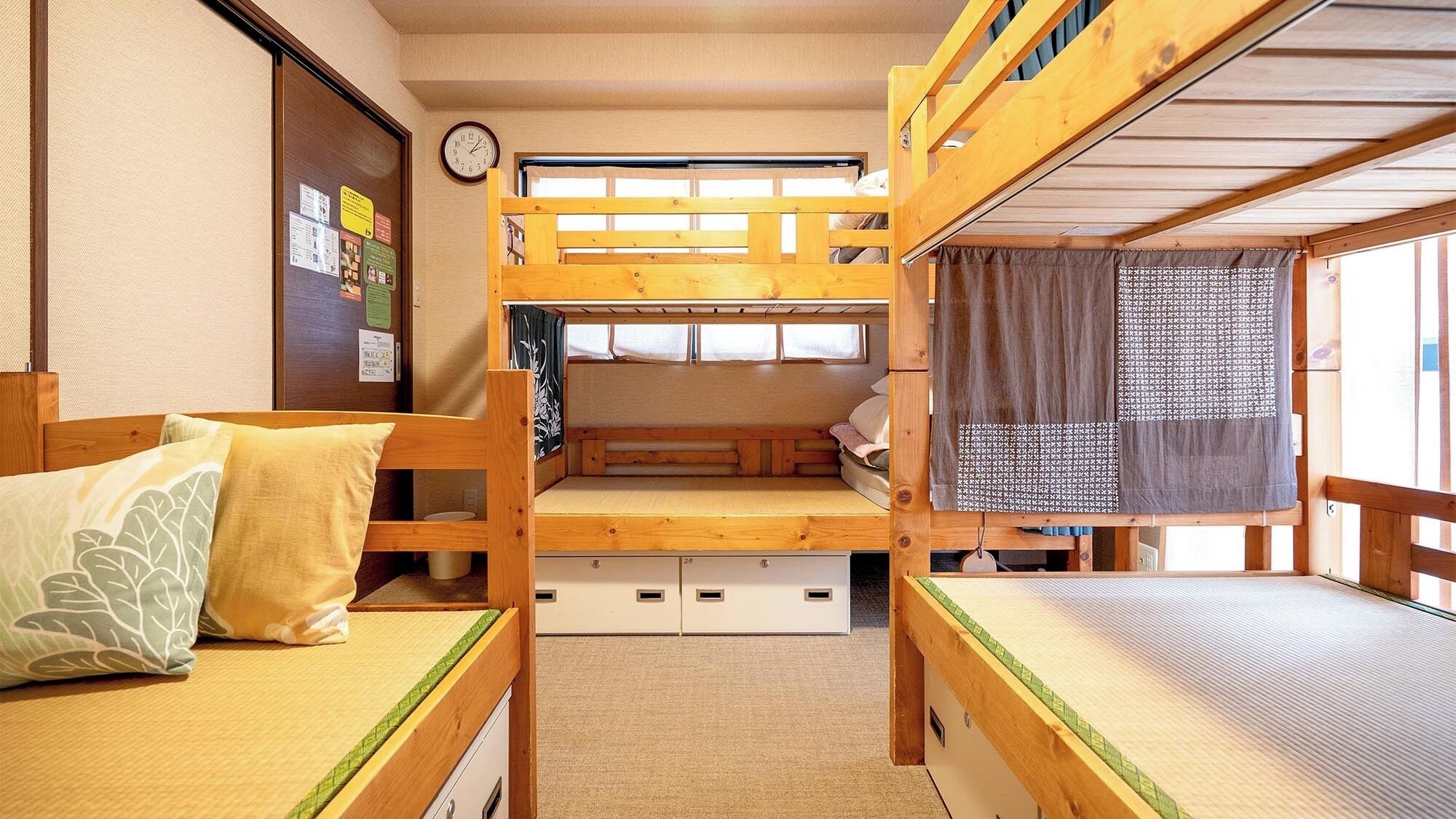 A bunk bed room with a wooden floor, a clock on the wall, and a window with a curtain.