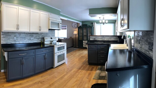A modern kitchen with dark cabinets, a black countertop, and a tiled backsplash.