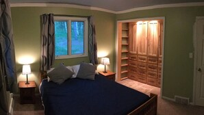 A bedroom with a bed, two bedside lamps, a window with curtains, and a built-in wooden closet.