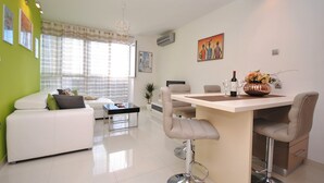 A modern living room with a white sofa, a dining area with a bar, and a kitchen in the background. - Apartment Antea - One Bedroom Apartment (Split)