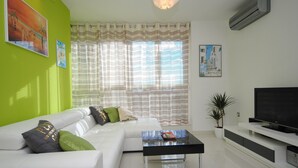 A modern living room with a white sofa, a glass coffee table, and a flat-screen TV on a white entertainment unit. - Apartment Antea - One Bedroom Apartment (Split)