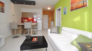 A modern living room with a white sofa, a black coffee table, and a kitchen in the background. - Apartment Antea - One Bedroom Apartment (Split)