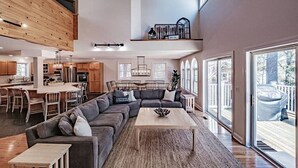 A spacious living area with a large sectional sofa, a coffee table, and a kitchen in the background. - MAINE WATERFRONT + MOUNTAIN COMPOUND • SLEEPS 50! (Bridgton)