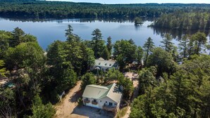 An aerial view of a house surrounded by dense forest and a lake. - MAINE WATERFRONT + MOUNTAIN COMPOUND • SLEEPS 50! (Bridgton)