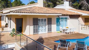 Une maison avec un toit en tuiles, une piscine et une terrasse avec des chaises.
