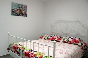 A bed with a floral bedspread and two pillows, a white metal headboard, and a painting on the wall. - Apartments Clementina Sunrise - Two-Bedroom Apartment with Terrace and Sea View (Orebic)