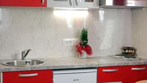 Una cucina compatta con mobili rossi, una lavastoviglie bianca e un piccolo angolo ristoro con una sedia.
