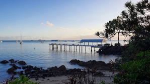 A coastal scene with a pier extending into calm waters, surrounded by rocks and greenery.
