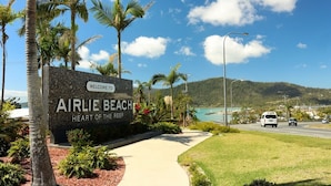 A sign welcoming visitors to Airlie Beach, with a view of the sea and mountains in the background.