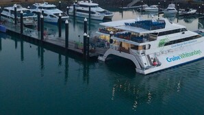 A ferry docked at a marina with a large boat named "Cruise Whitsundays" and another boat named "Great Barrier Reef Adventures" in the background.