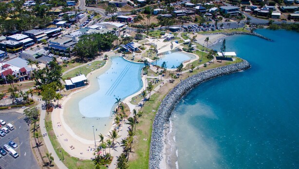 An aerial view of a coastal resort with a large swimming pool, beach, and a rocky shoreline.