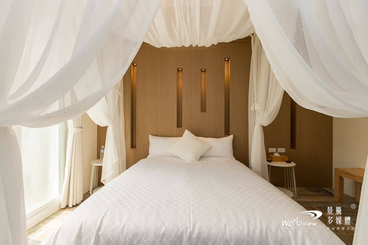 A bedroom with a large bed, white bedding, and sheer curtains.