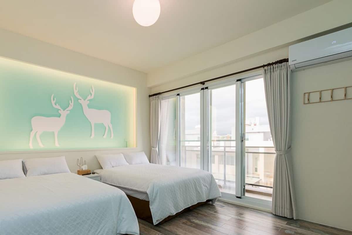 A modern hotel room with two beds, a large window with curtains, and a wall-mounted artwork of deer.
