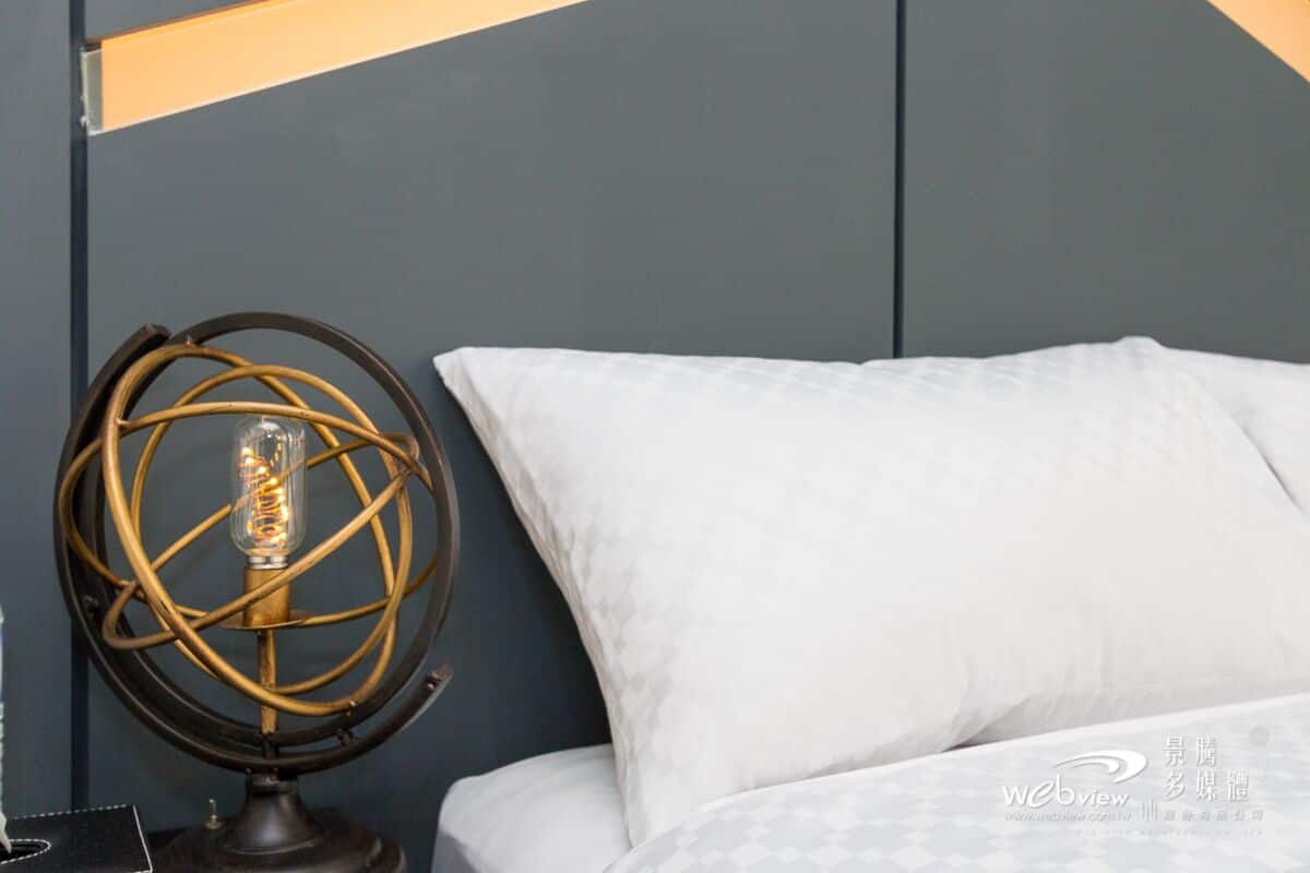 A bed with white bedding and a globe lamp on a bedside table.