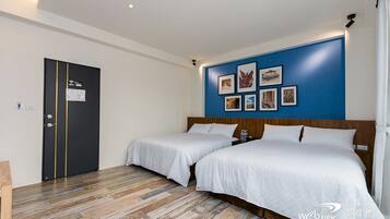 A hotel room with two beds, a blue accent wall with framed pictures, a wooden headboard, and a door with a sign.
